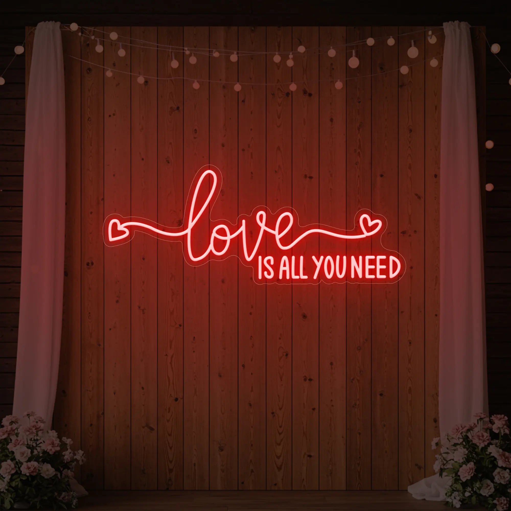 Photo of the 'Love Is All You Need' neon sign glowing in red against a styled interior wall.