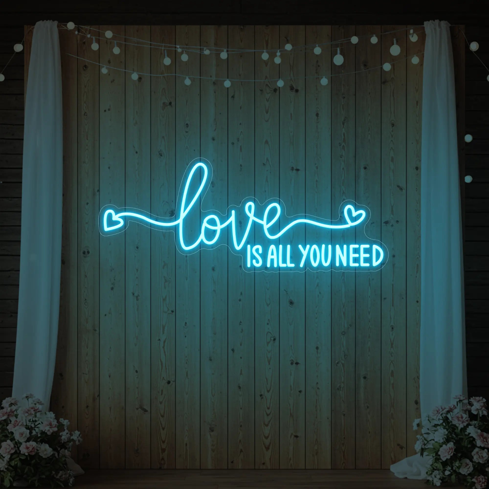 Photo of the 'Love Is All You Need' neon sign glowing in ice blue against a styled interior wall.