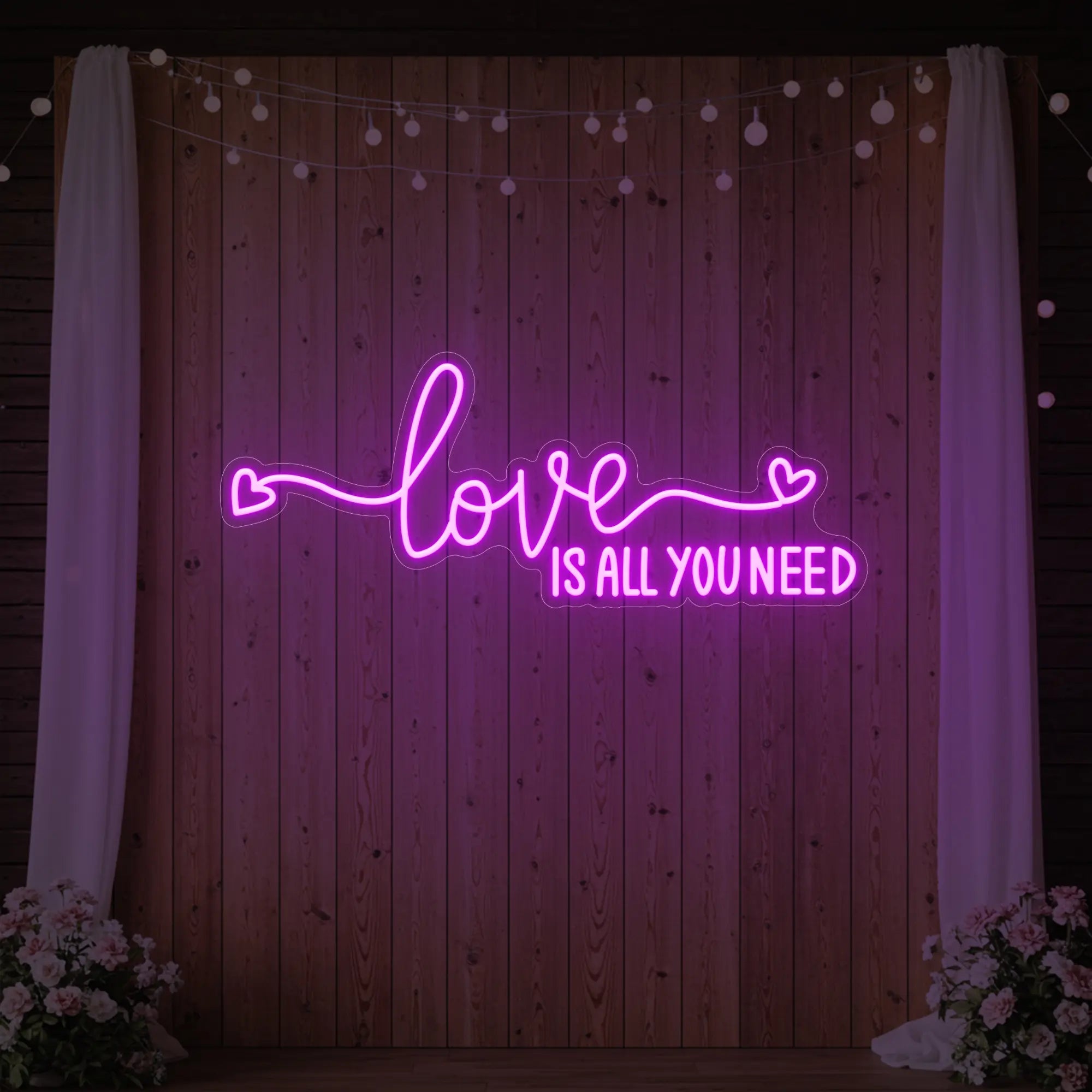 Photo of the 'Love Is All You Need' neon sign glowing in deep pink against a styled interior wall.