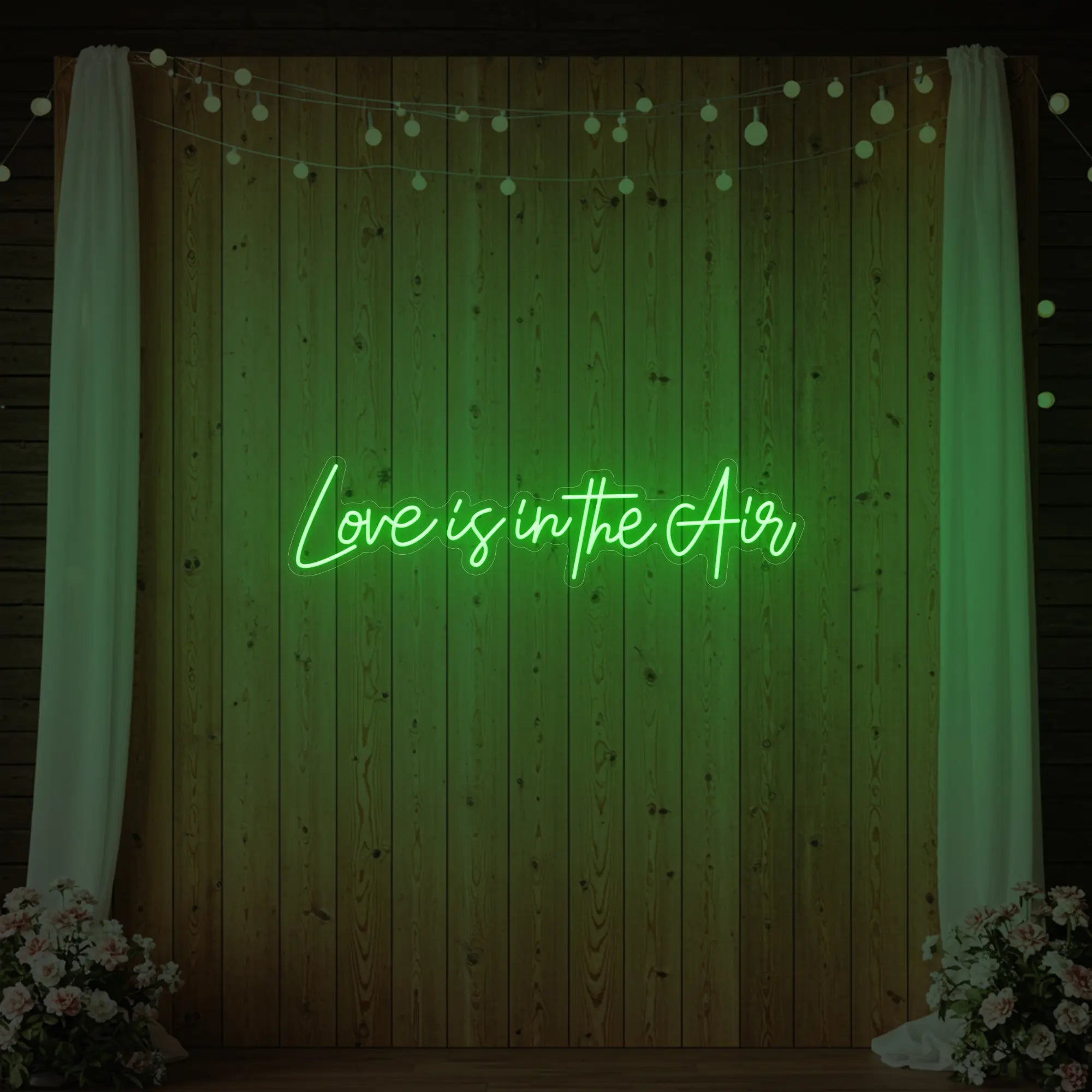 Photo of the 'Love Is In The Air' neon sign glowing in green against a styled interior wall.