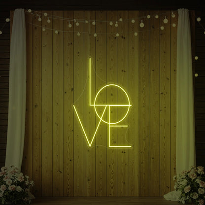 Photo of the 'LOVE' neon sign glowing in lemon yellow against a styled interior wall.