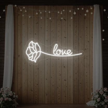 Photo of the 'Just Love Rose' neon sign glowing in cool white against a styled interior wall.