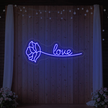 Photo of the 'Just Love Rose' neon sign glowing in deep blue against a styled interior wall.