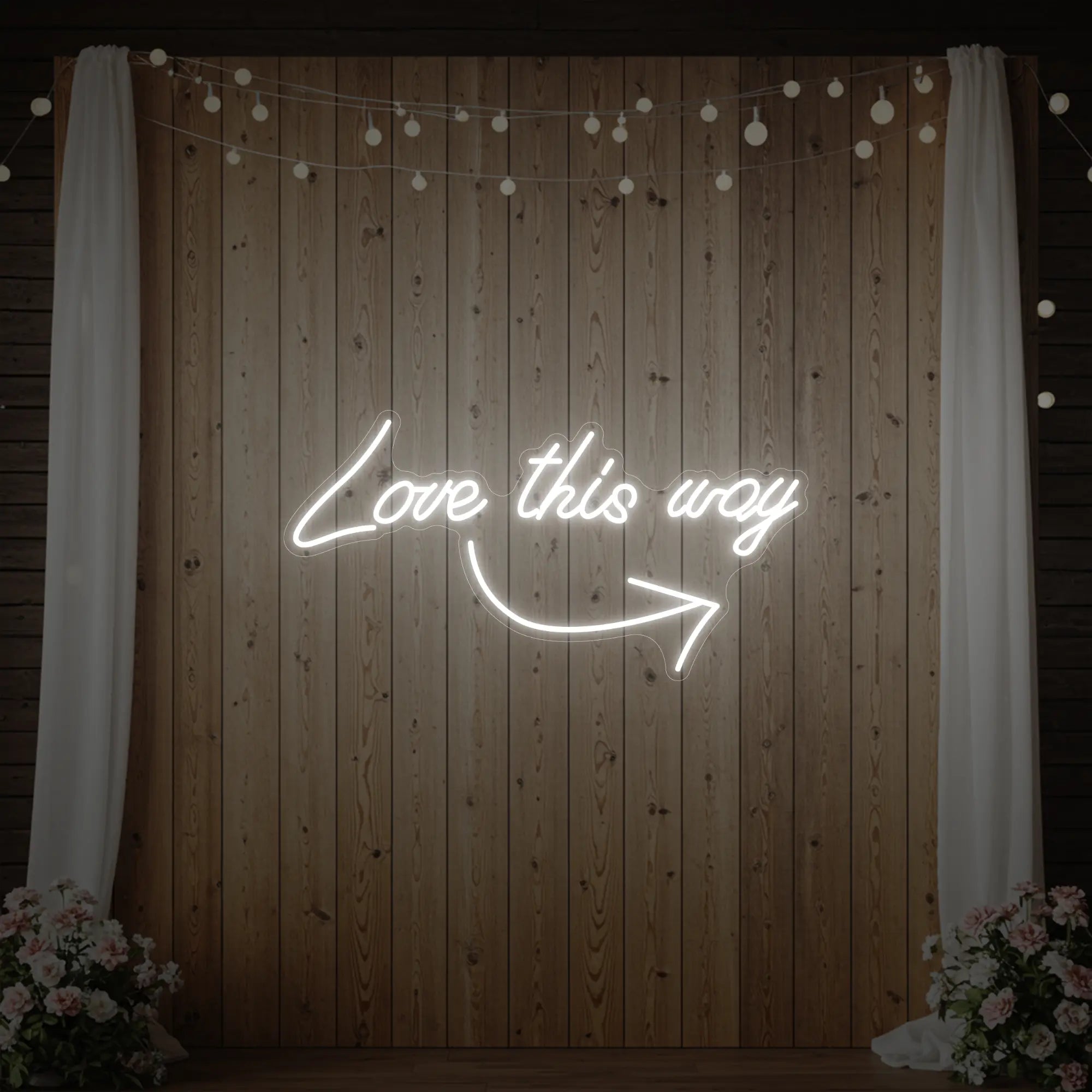 Photo of the 'Love This Way' neon sign glowing in cool white against a styled interior wall.