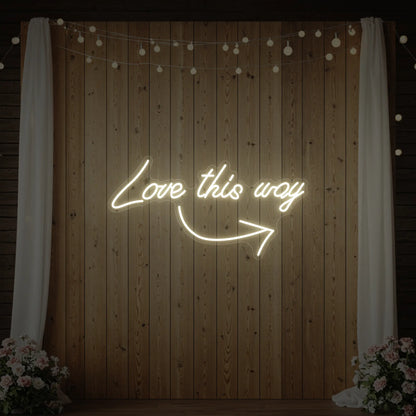 Photo of the 'Love This Way' neon sign glowing in warm white against a styled interior wall.
