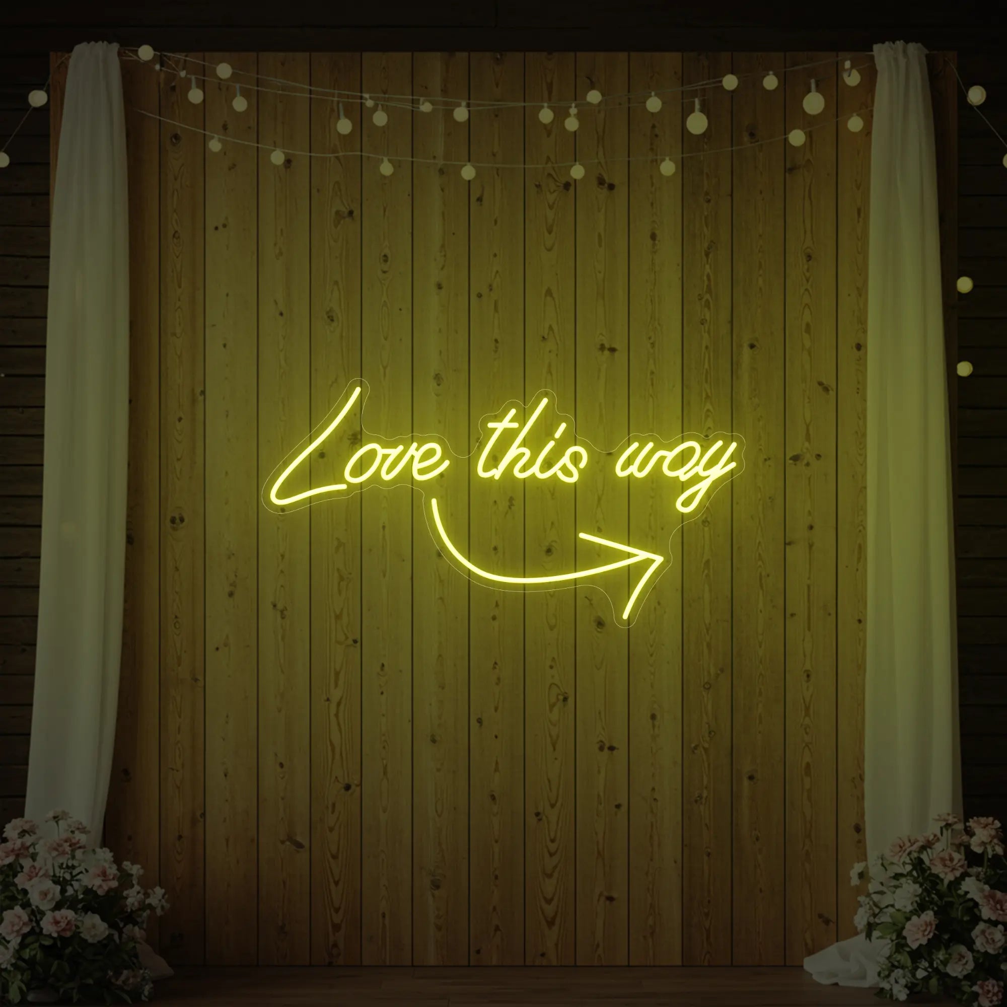 Photo of the 'Love This Way' neon sign glowing in lemon yellow against a styled interior wall.