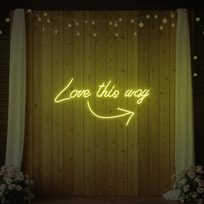 Photo of the 'Love This Way' neon sign glowing in lemon yellow against a styled interior wall.