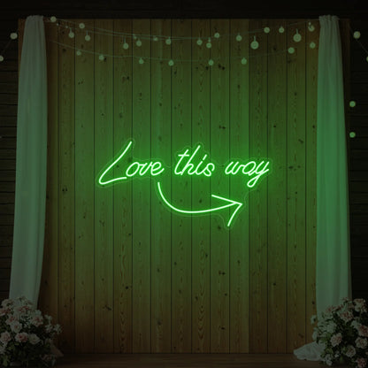 Photo of the 'Love This Way' neon sign glowing in green against a styled interior wall.