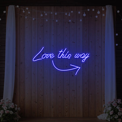 Photo of the 'Love This Way' neon sign glowing in deep blue against a styled interior wall.