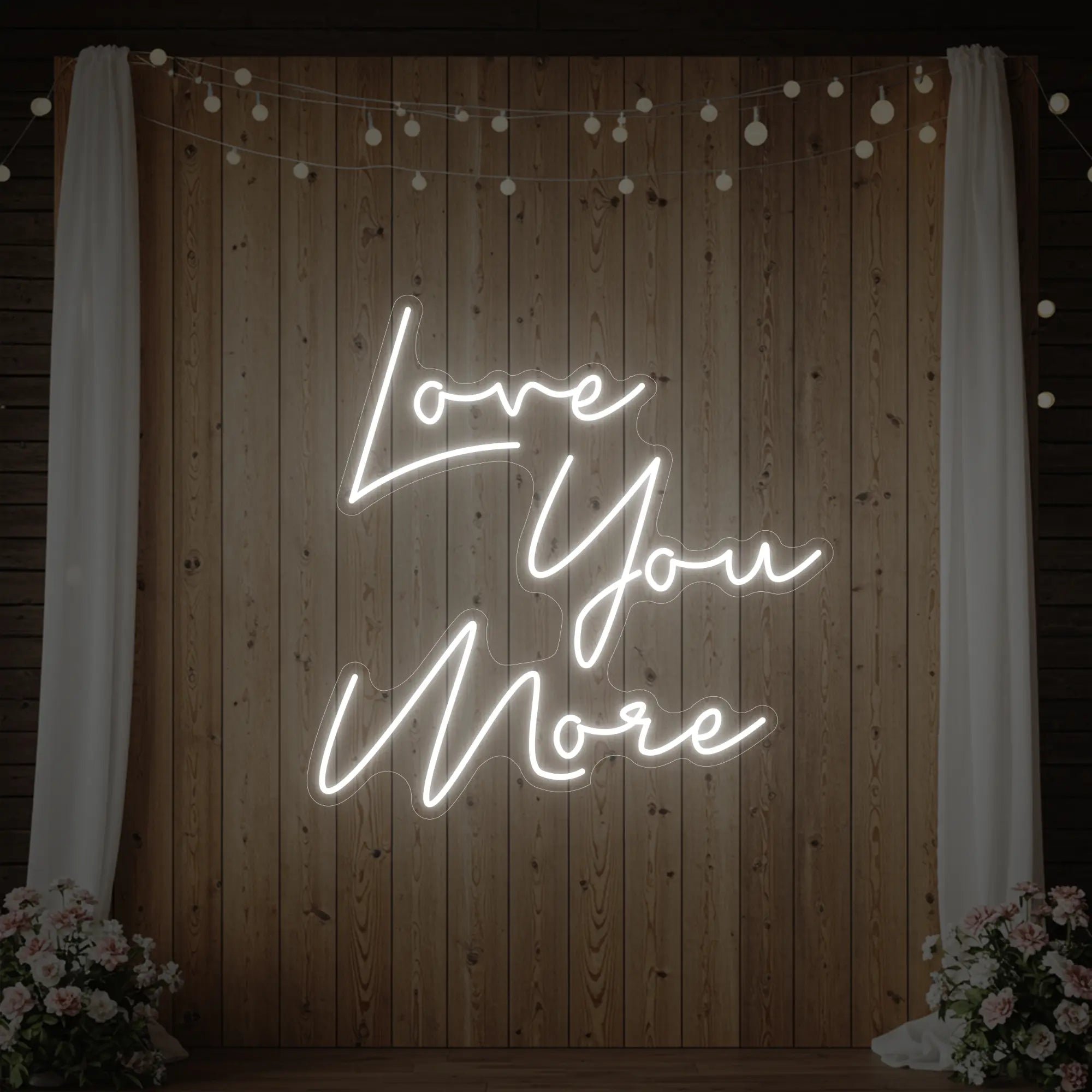 Photo of the 'Love You More' neon sign glowing in cool white against a styled interior wall.