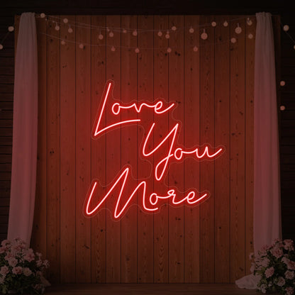 Photo of the 'Love You More' neon sign glowing in red against a styled interior wall.