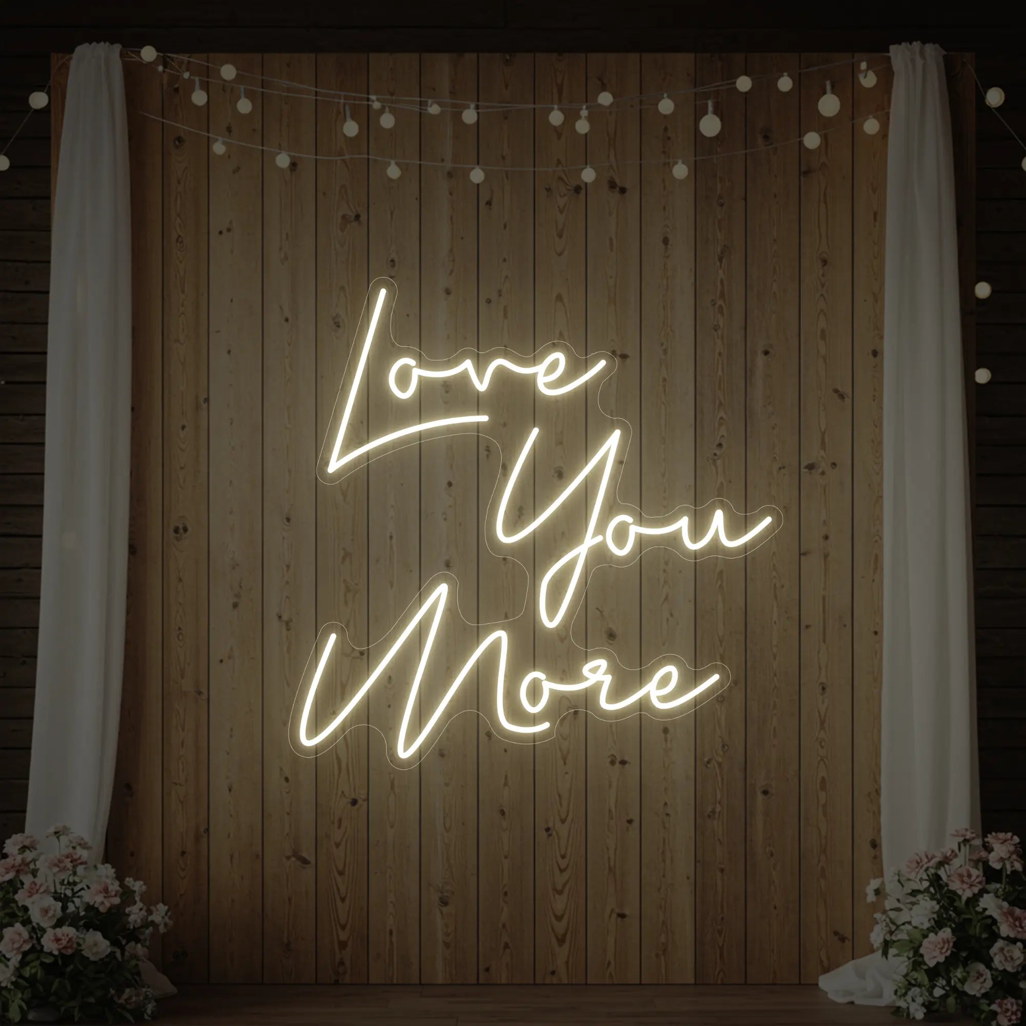 Photo of the 'Love You More' neon sign glowing in warm white against a styled interior wall.