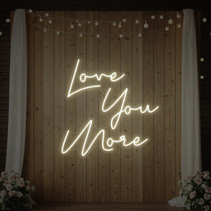 Photo of the 'Love You More' neon sign glowing in warm white against a styled interior wall.