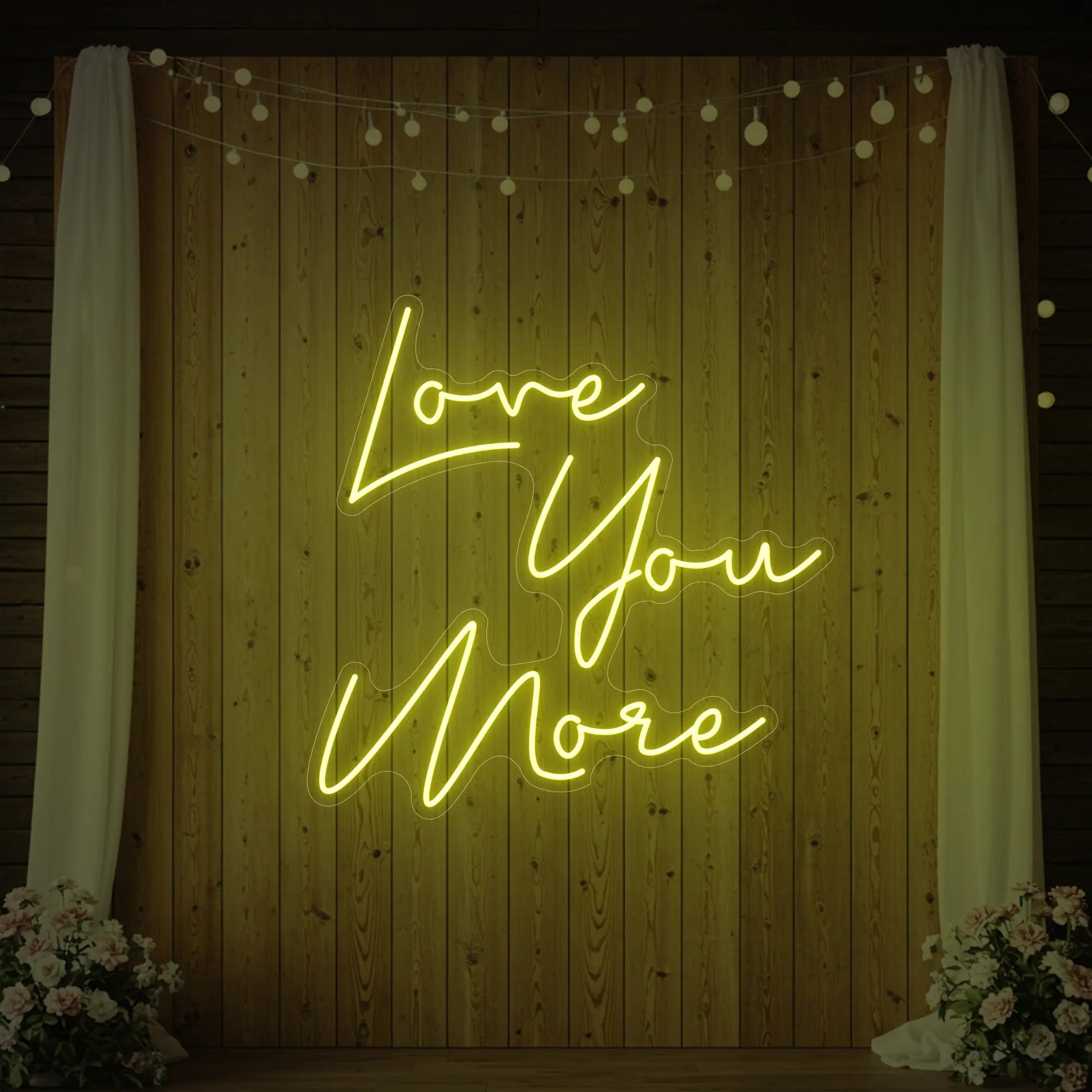 Photo of the 'Love You More' neon sign glowing in lemon yellow against a styled interior wall.