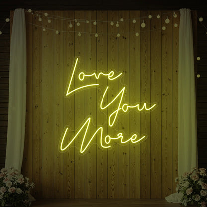 Photo of the 'Love You More' neon sign glowing in lemon yellow against a styled interior wall.
