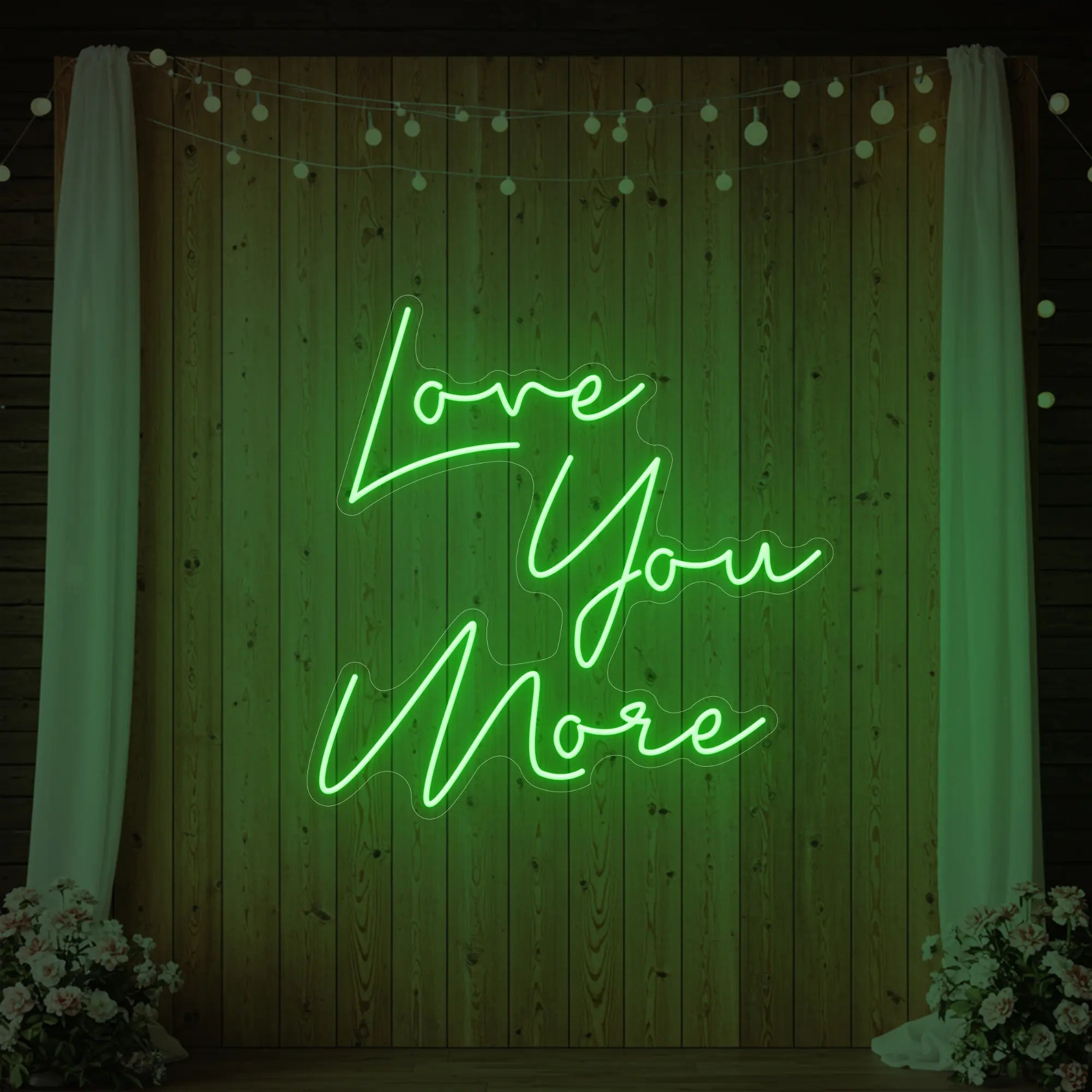 Photo of the 'Love You More' neon sign glowing in green against a styled interior wall.