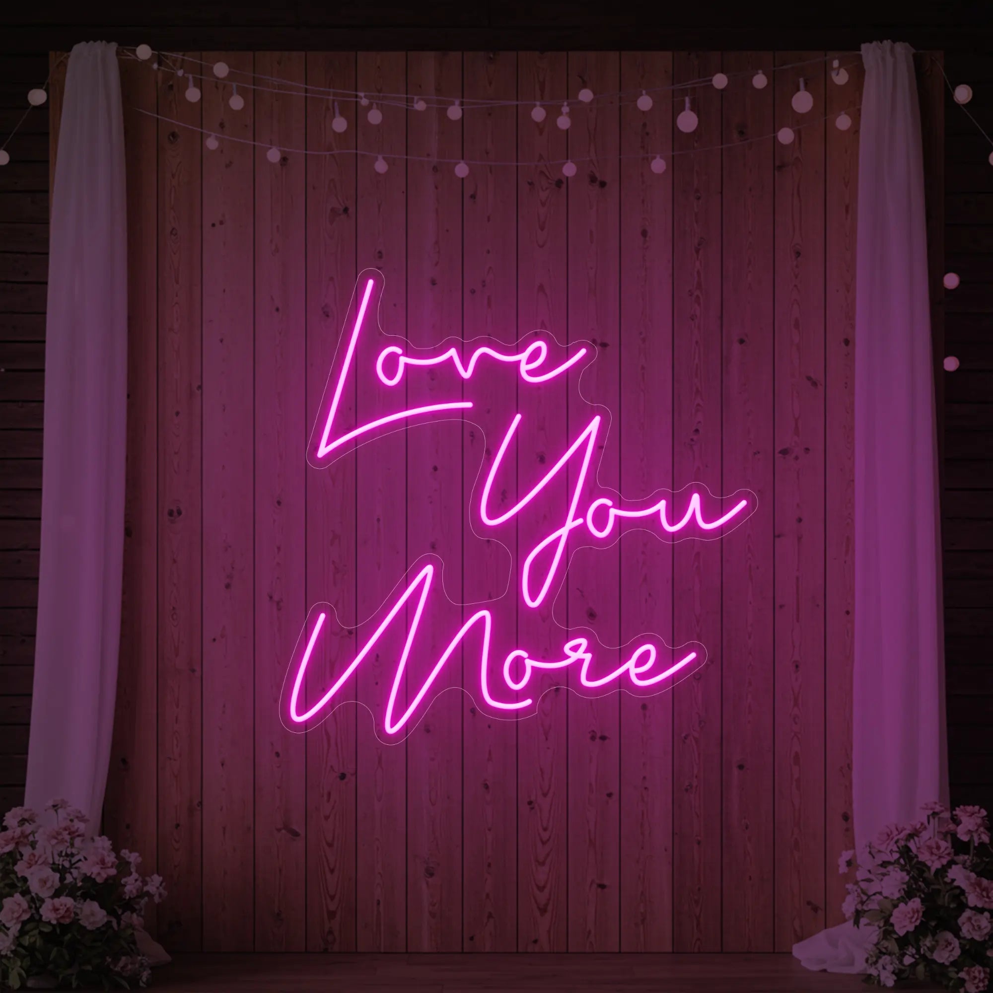 Photo of the 'Love You More' neon sign glowing in light pink against a styled interior wall.
