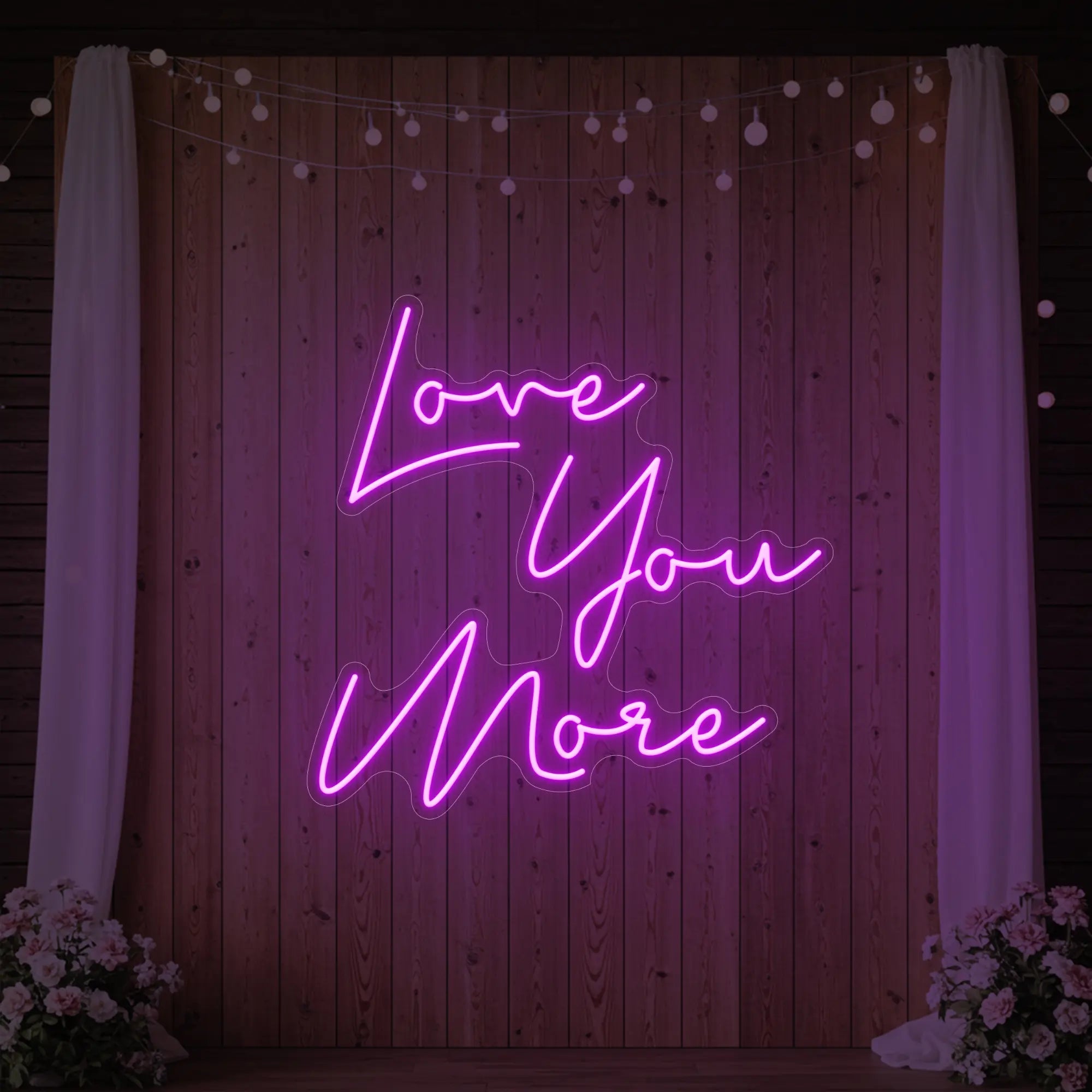 Photo of the 'Love You More' neon sign glowing in deep pink against a styled interior wall.