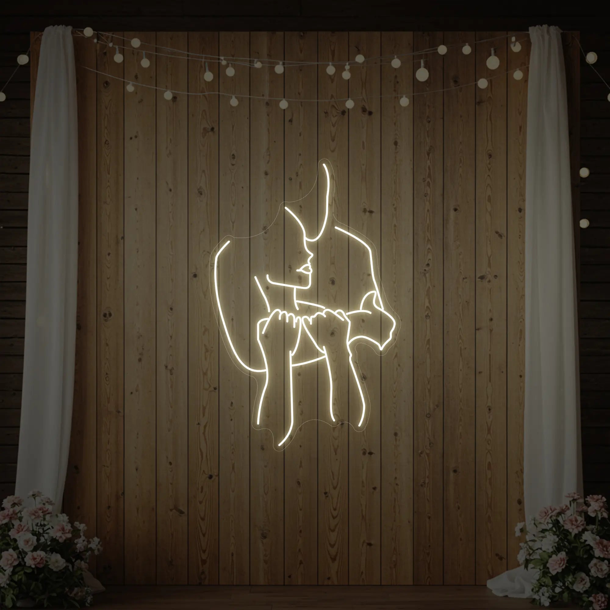 Photo of the 'Lovers Holding Each Other' neon sign glowing in warm white against a styled interior wall.