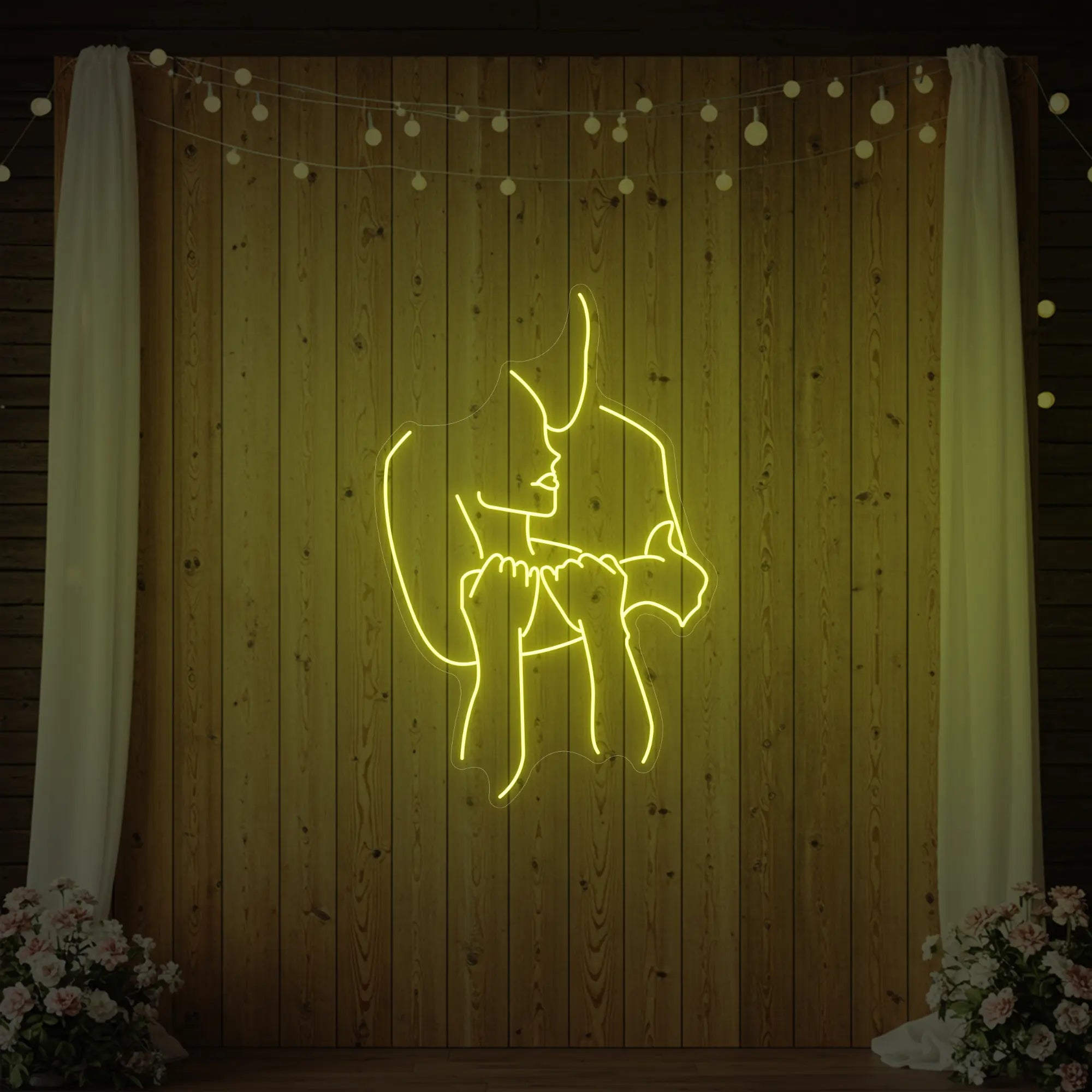 Photo of the 'Lovers Holding Each Other' neon sign glowing in lemon yellow against a styled interior wall.