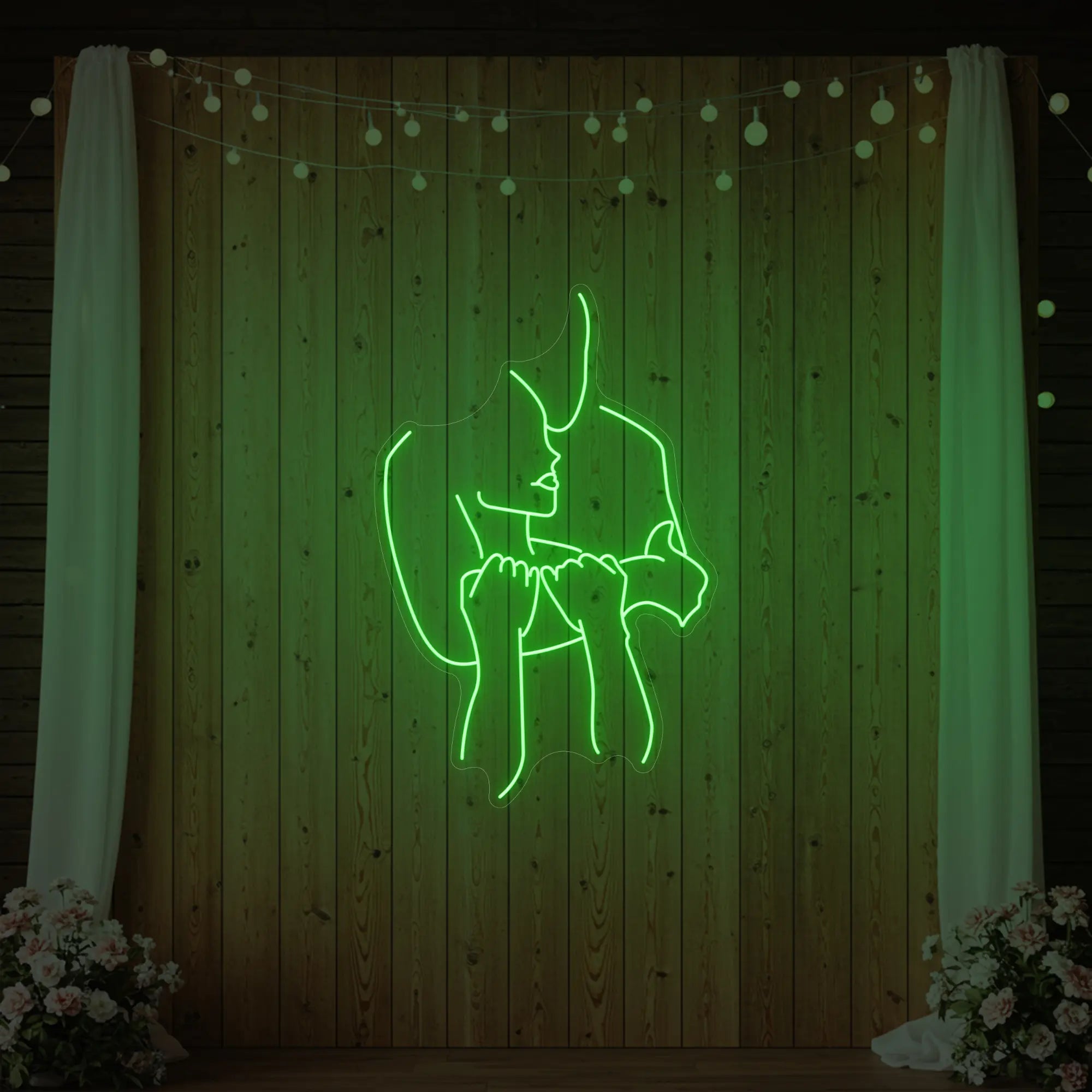 Photo of the 'Lovers Holding Each Other' neon sign glowing in green against a styled interior wall.