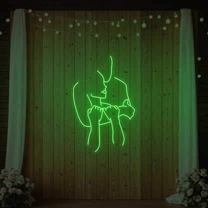 Photo of the 'Lovers Holding Each Other' neon sign glowing in green against a styled interior wall.