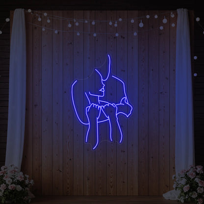 Photo of the 'Lovers Holding Each Other' neon sign glowing in deep blue against a styled interior wall.