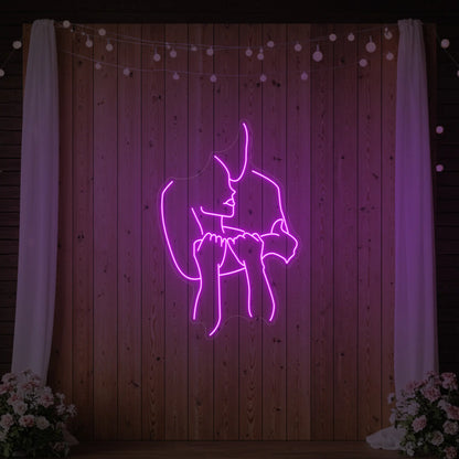 Photo of the 'Lovers Holding Each Other' neon sign glowing in deep pink against a styled interior wall.