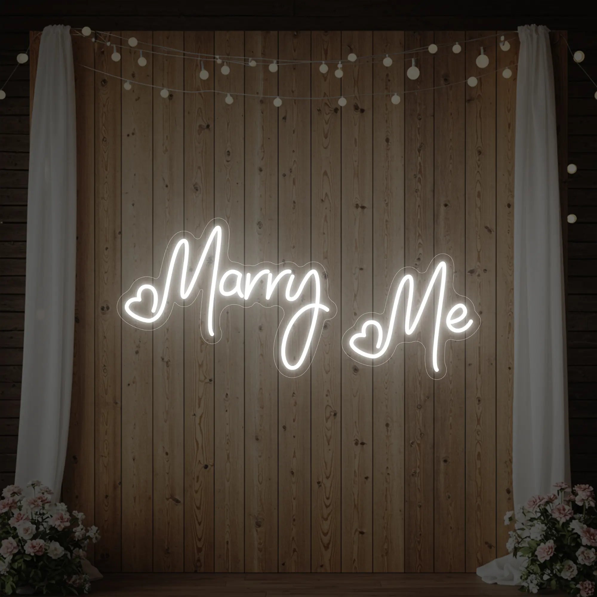 Photo of the 'Marry Me' neon sign glowing in cool white against a styled interior wall.