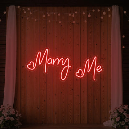 Photo of the 'Marry Me' neon sign glowing in red against a styled interior wall.