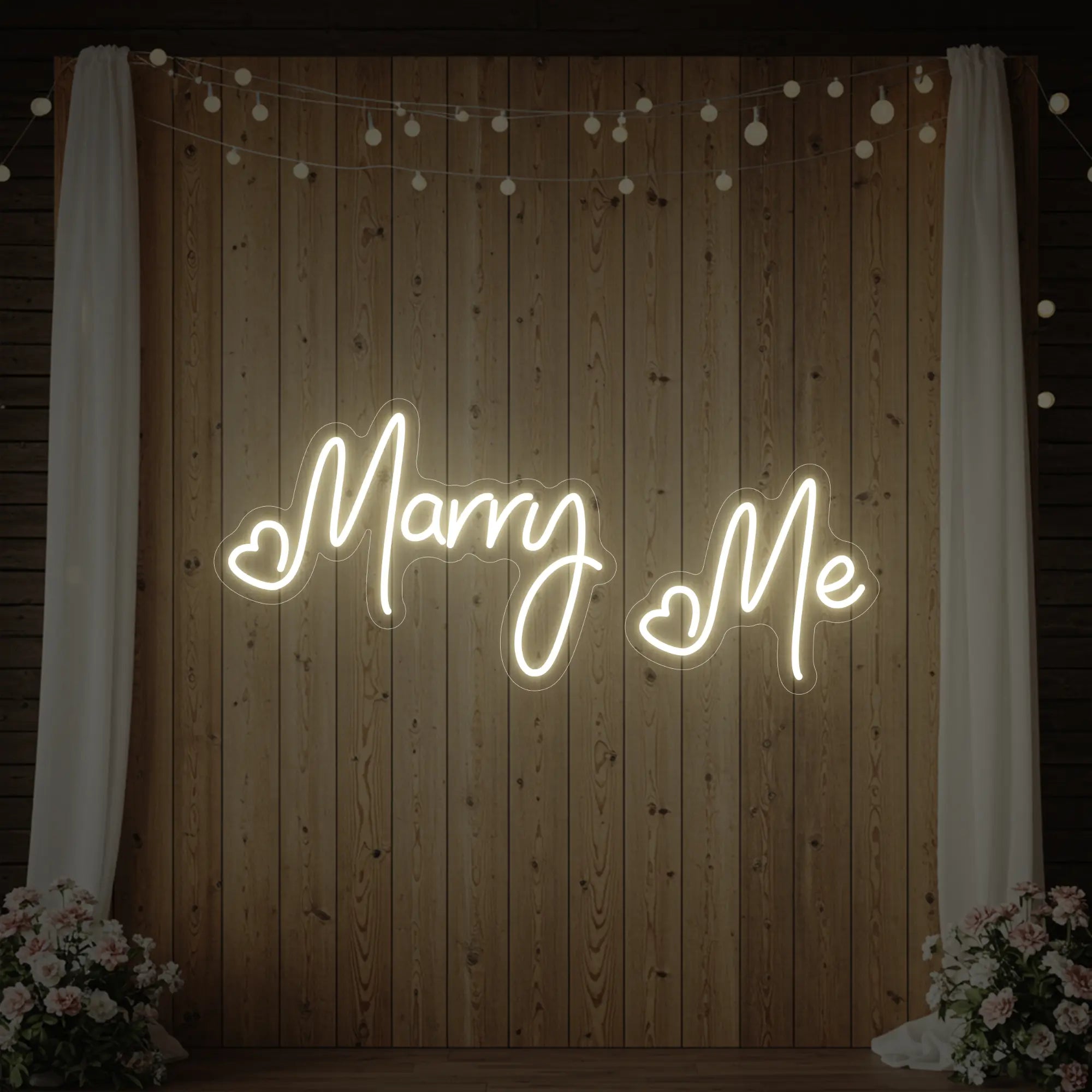 Photo of the 'Marry Me' neon sign glowing in warm white against a styled interior wall.