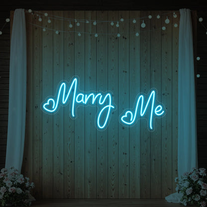 Photo of the 'Marry Me' neon sign glowing in ice blue against a styled interior wall.