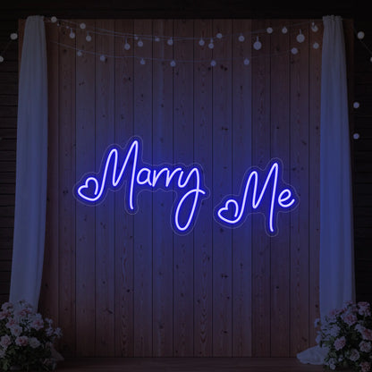 Photo of the 'Marry Me' neon sign glowing in deep blue against a styled interior wall.