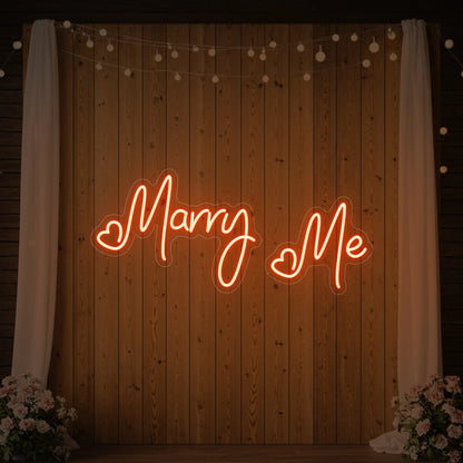 Photo of the 'Marry Me' neon sign glowing in golden yellow against a styled interior wall.