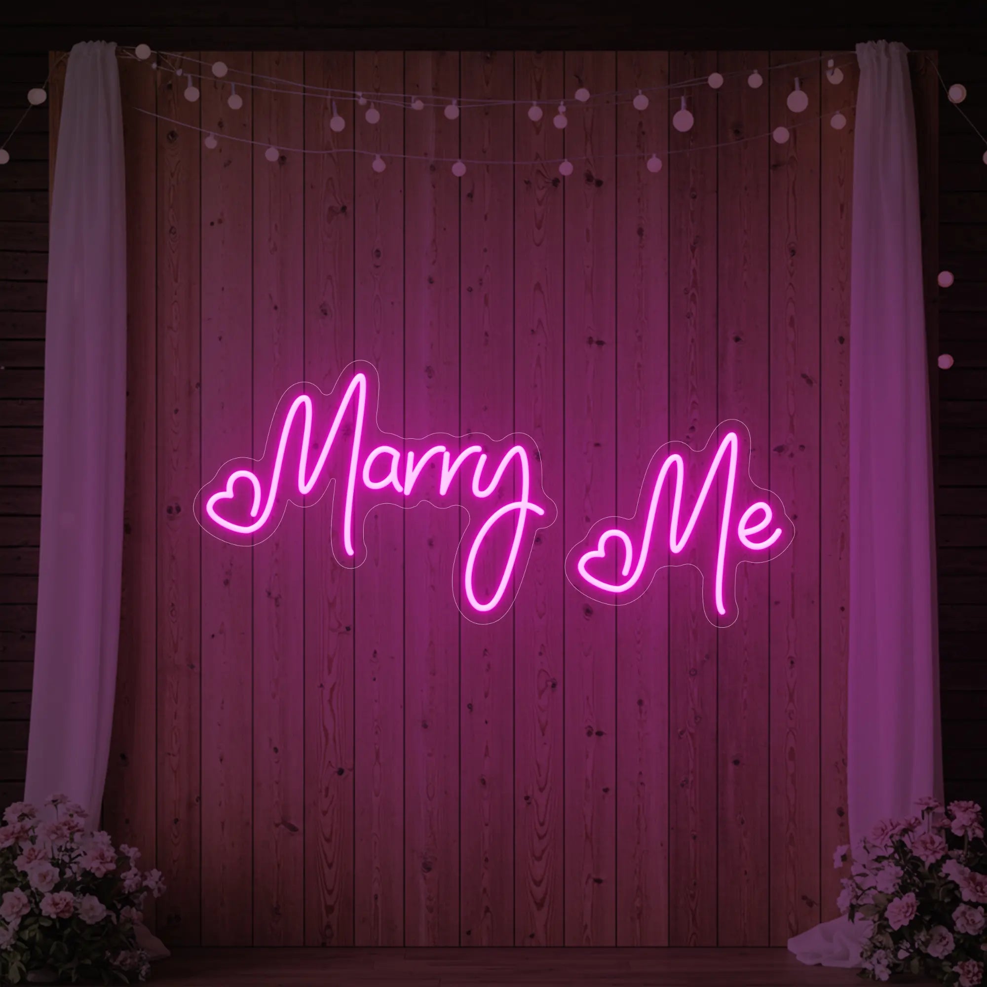 Photo of the 'Marry Me' neon sign glowing in light pink against a styled interior wall.