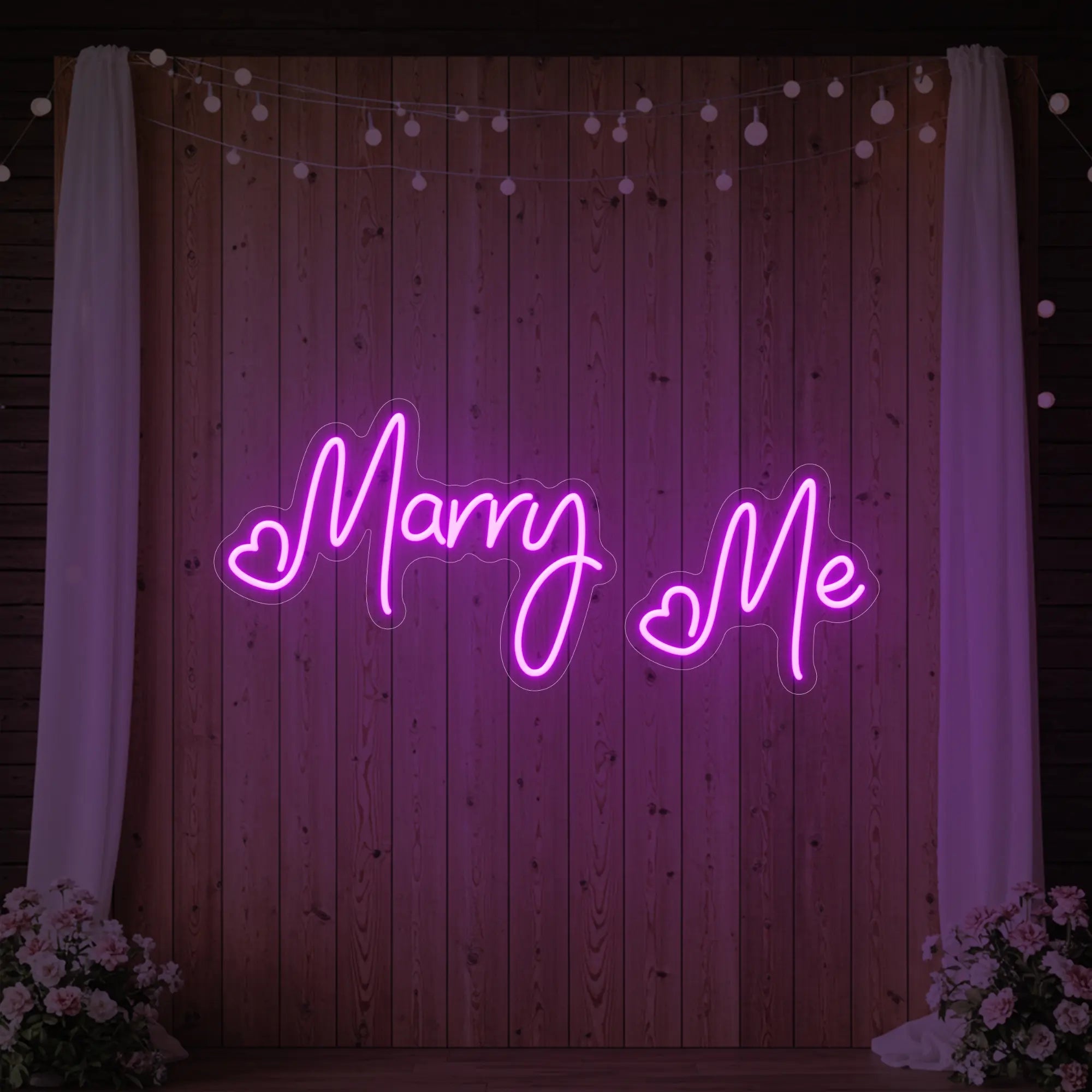Photo of the 'Marry Me' neon sign glowing in deep pink against a styled interior wall.