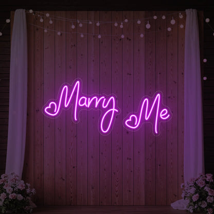 Photo of the 'Marry Me' neon sign glowing in deep pink against a styled interior wall.