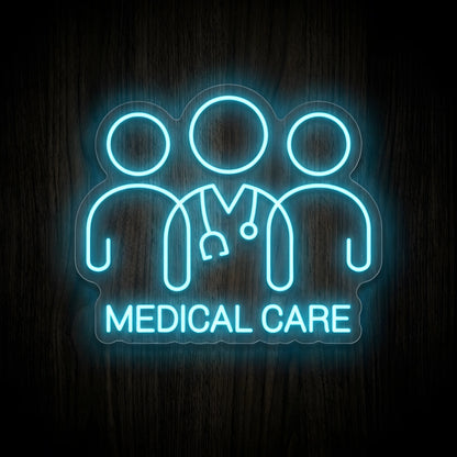 Medical Care Team LED Neon Sign featuring three healthcare figures with a central stethoscope and glowing cyan-blue Medical Care lettering on clear acrylic backing against a dark wooden wall.