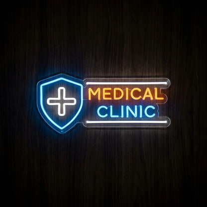 Medical Clinic Shield LED Neon Sign featuring a blue shield with a white medical cross, orange MEDICAL lettering, and blue CLINIC text on clear acrylic backing against a dark wooden wall.