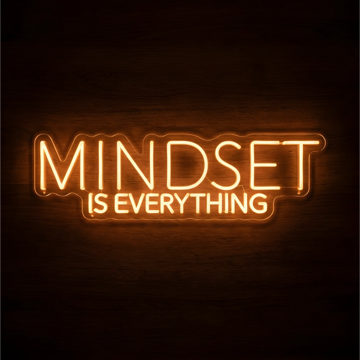 “MINDSET IS EVERYTHING” LED Neon Sign glowing in warm amber uppercase letters, with “MINDSET” larger above “IS EVERYTHING,” on clear acrylic against a dark wood background, suited to home offices and creative workspaces.