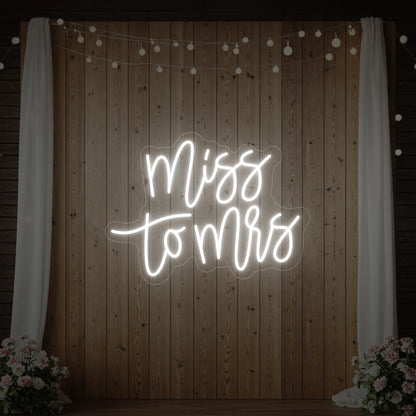 Photo of the 'Miss to Mrs' neon sign glowing in cool white against a styled interior wall.