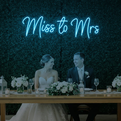 Photo of the 'Miss to Mrs' neon sign glowing in ice blue against a styled interior wall.