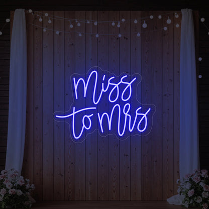 Photo of the 'Miss to Mrs' neon sign glowing in deep blue against a styled interior wall.