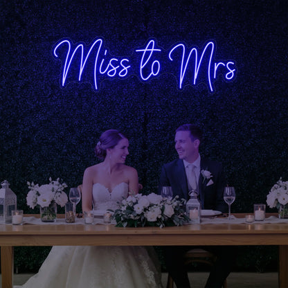 Photo of the 'Miss to Mrs' neon sign glowing in deep blue against a styled interior wall.