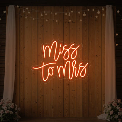 Photo of the 'Miss to Mrs' neon sign glowing in golden yellow against a styled interior wall.