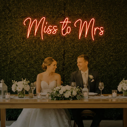 Photo of the 'Miss to Mrs' neon sign glowing in golden yellow against a styled interior wall.