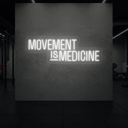  'Movement Is Medicine' neon sign glowing in cool white against a styled interior wall.