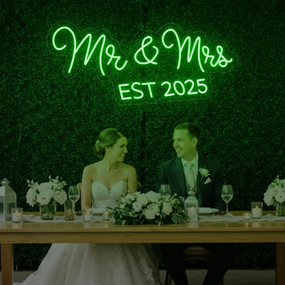 Photo of the 'Mr & Mrs EST' neon sign glowing in green against a styled interior wall.