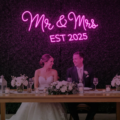 Photo of the 'Mr & Mrs EST' neon sign glowing in light pink against a styled interior wall.