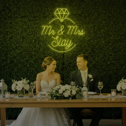 Photo of the 'Mr & Mrs EST' neon sign glowing in lemon yellow against a styled interior wall.